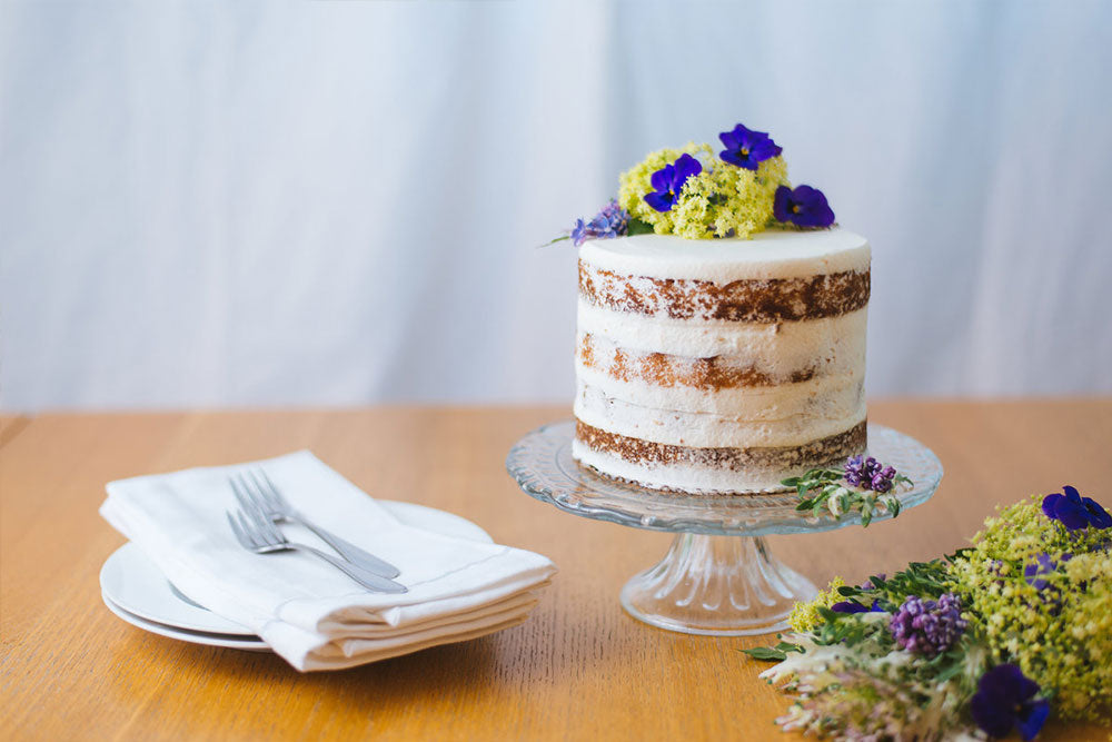 Photo of a naked cake garnished with flowers on a cake stand