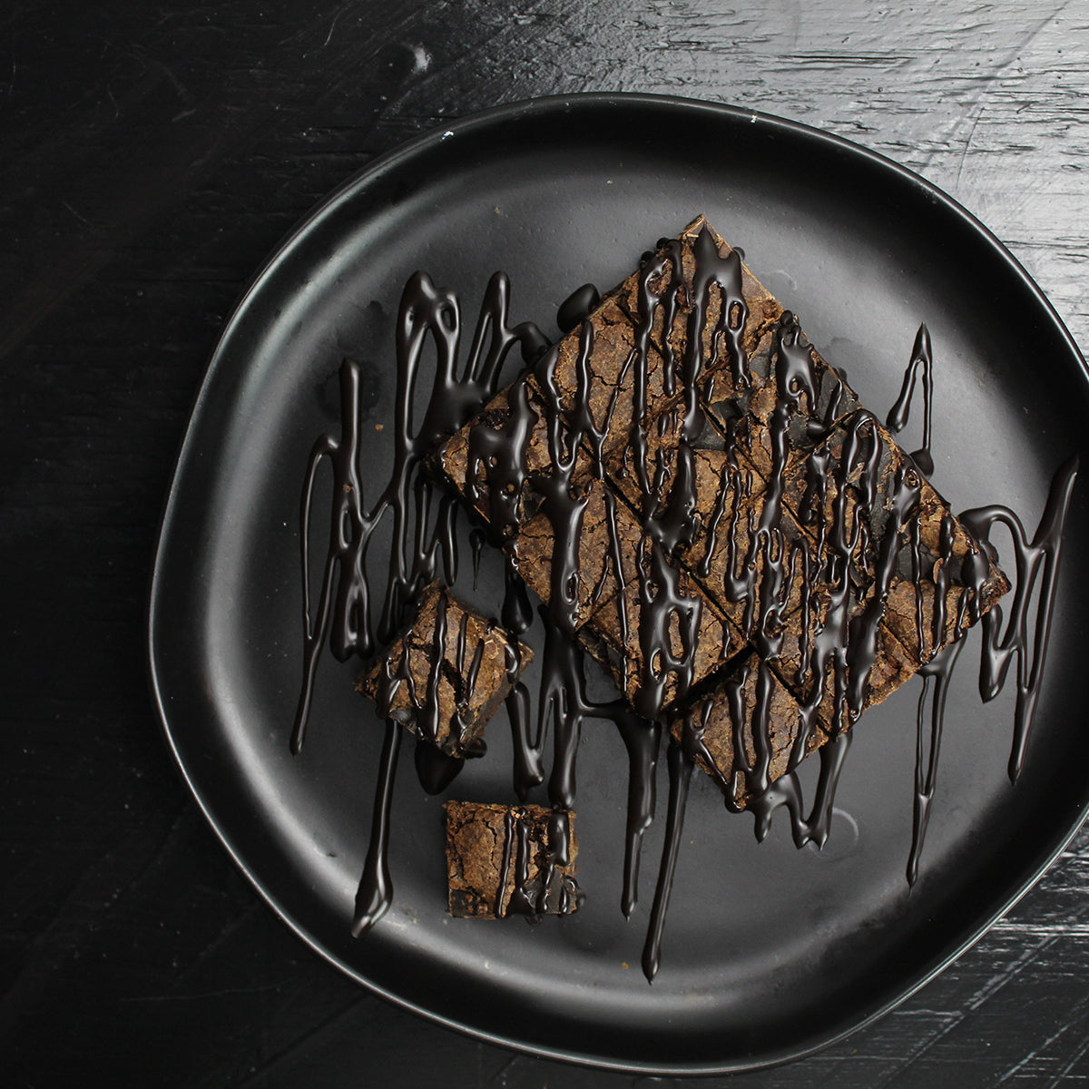 brownie bites drizzled with chocolate sauce on black plate