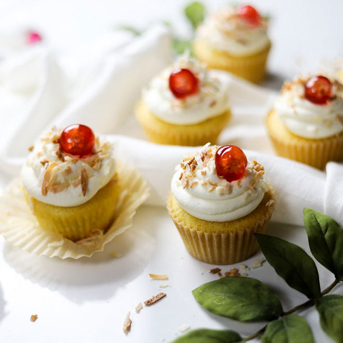 Image of Piña Colada Cupcakes garnished with sweetened coconut flakes and red cherry berries.
