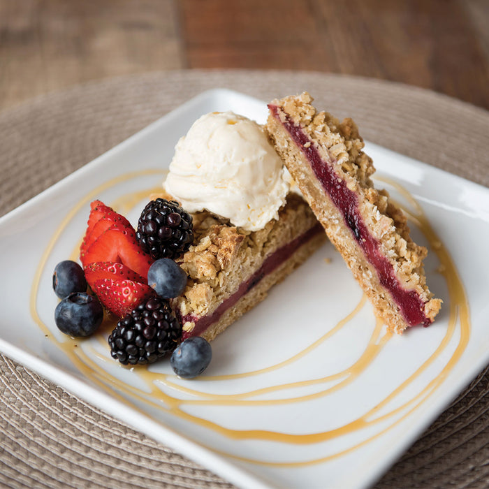 Triple berry crumble bar plated with fresh fruit and ice cream